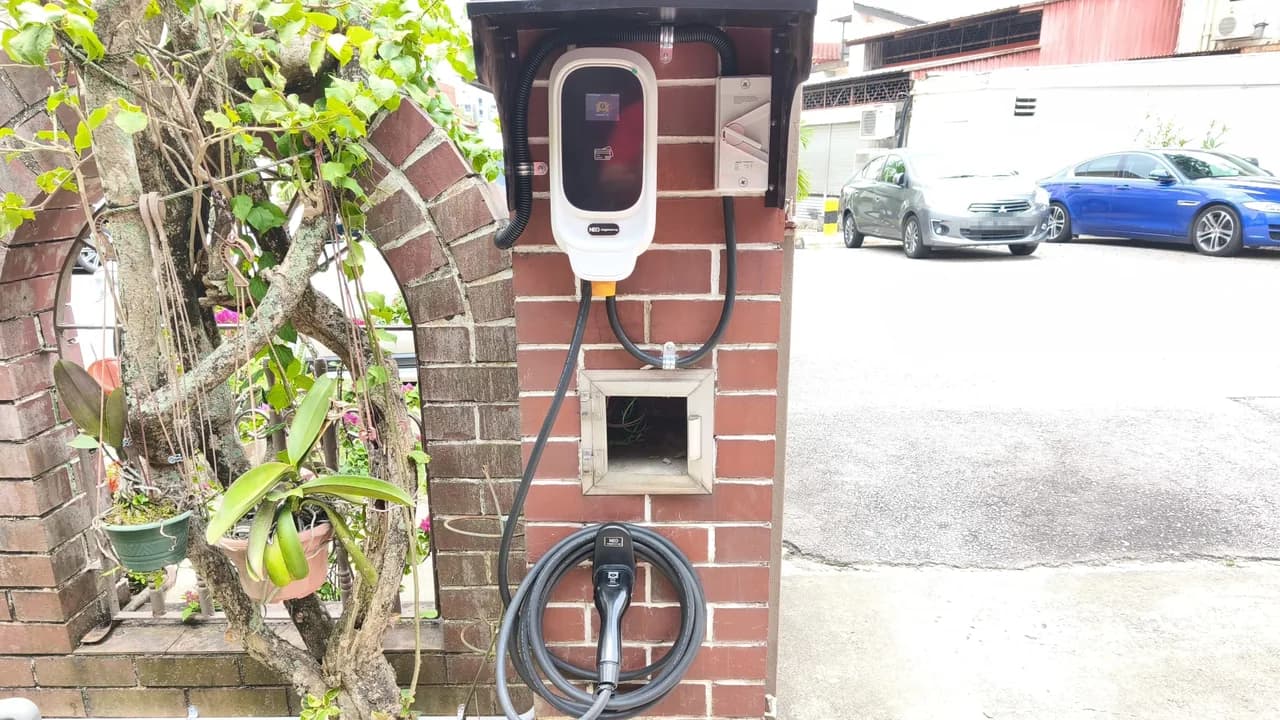 NEG wall charger under a small canopy on a red brick gate pillar, an isolator beside it and the cable coiled below.