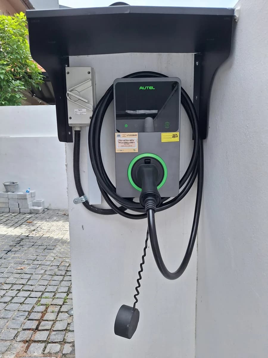 A dark Autel charger with a green ring, under a black steel weather hood with an isolator beside it.