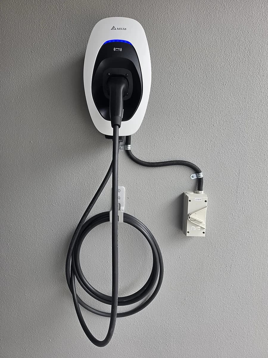 A white Delta charger with a blue status light and its connector docked, the cable looped on a wall hook.