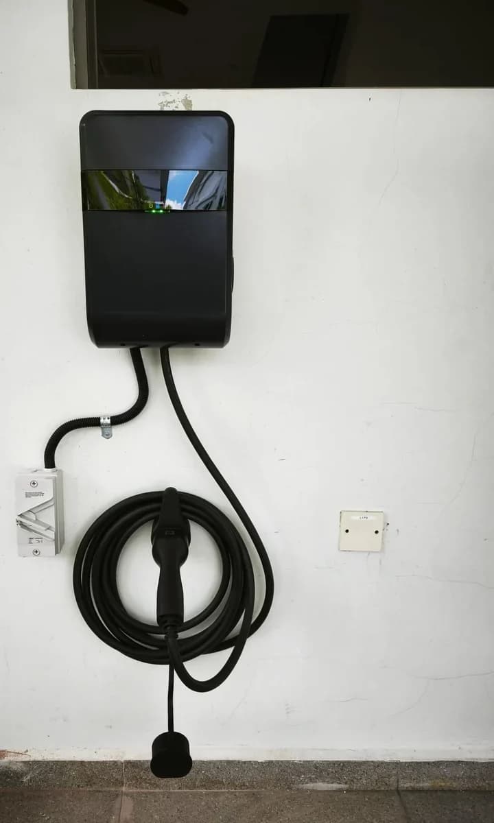 A dark grey wall charger below a window opening, its cable coiled on a holster bracket.