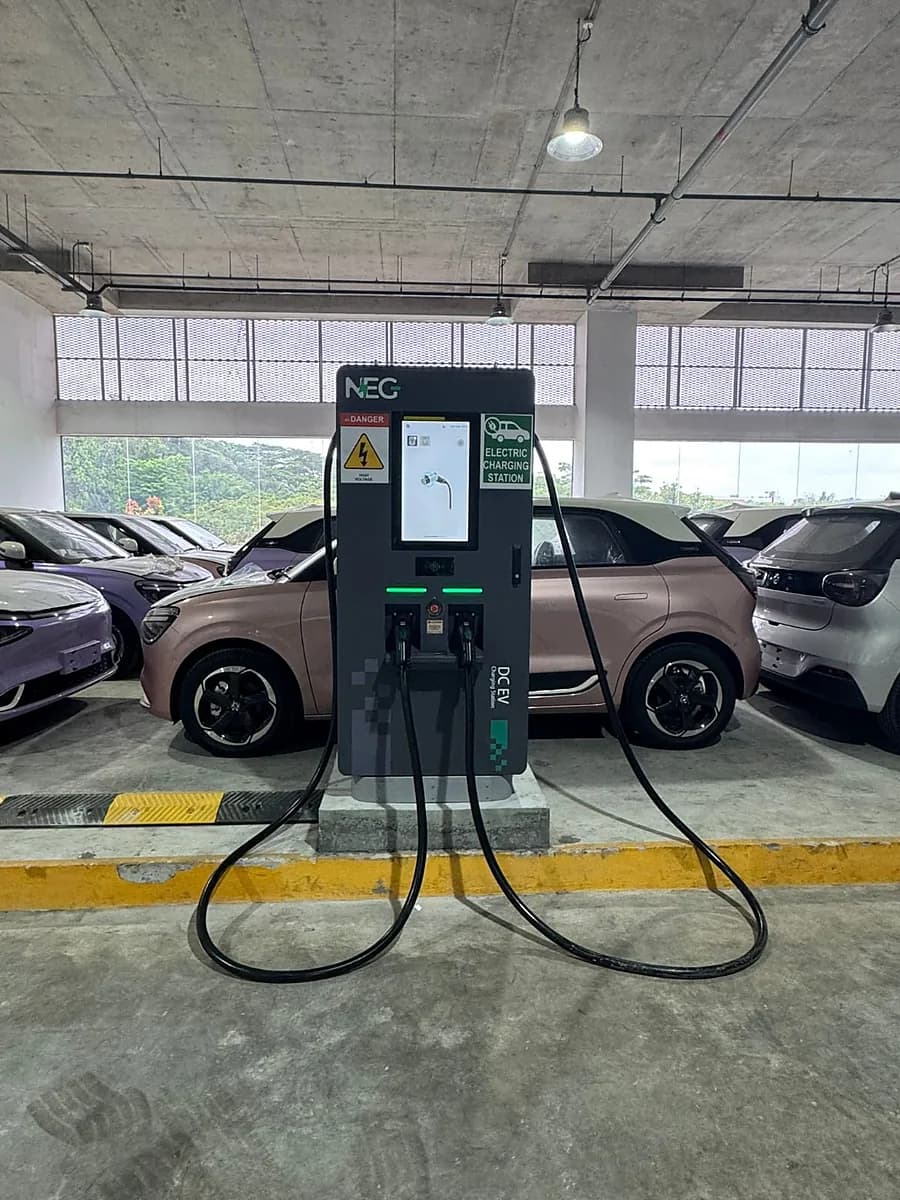 A floor-standing DC charger with two cables and a lit screen, in a covered car park.