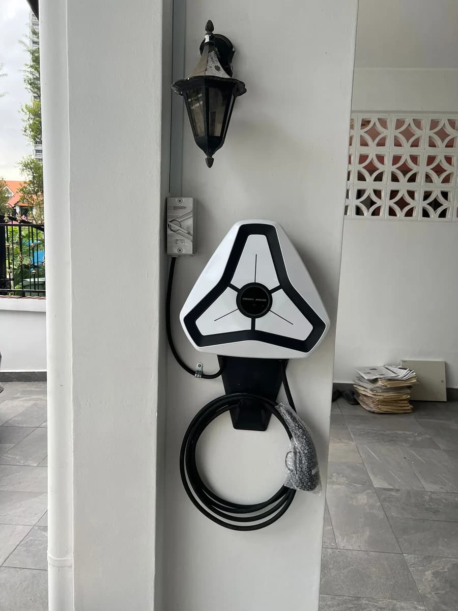 A white triangular Omoda charger on a pillar beneath a carriage lamp, an isolator above it.