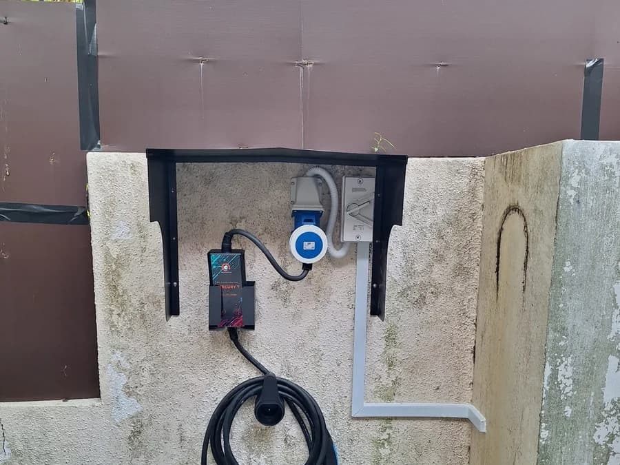 A Mercury 7 portable charger on a wall bracket, plugged into a blue industrial socket, with the cable coiled below.