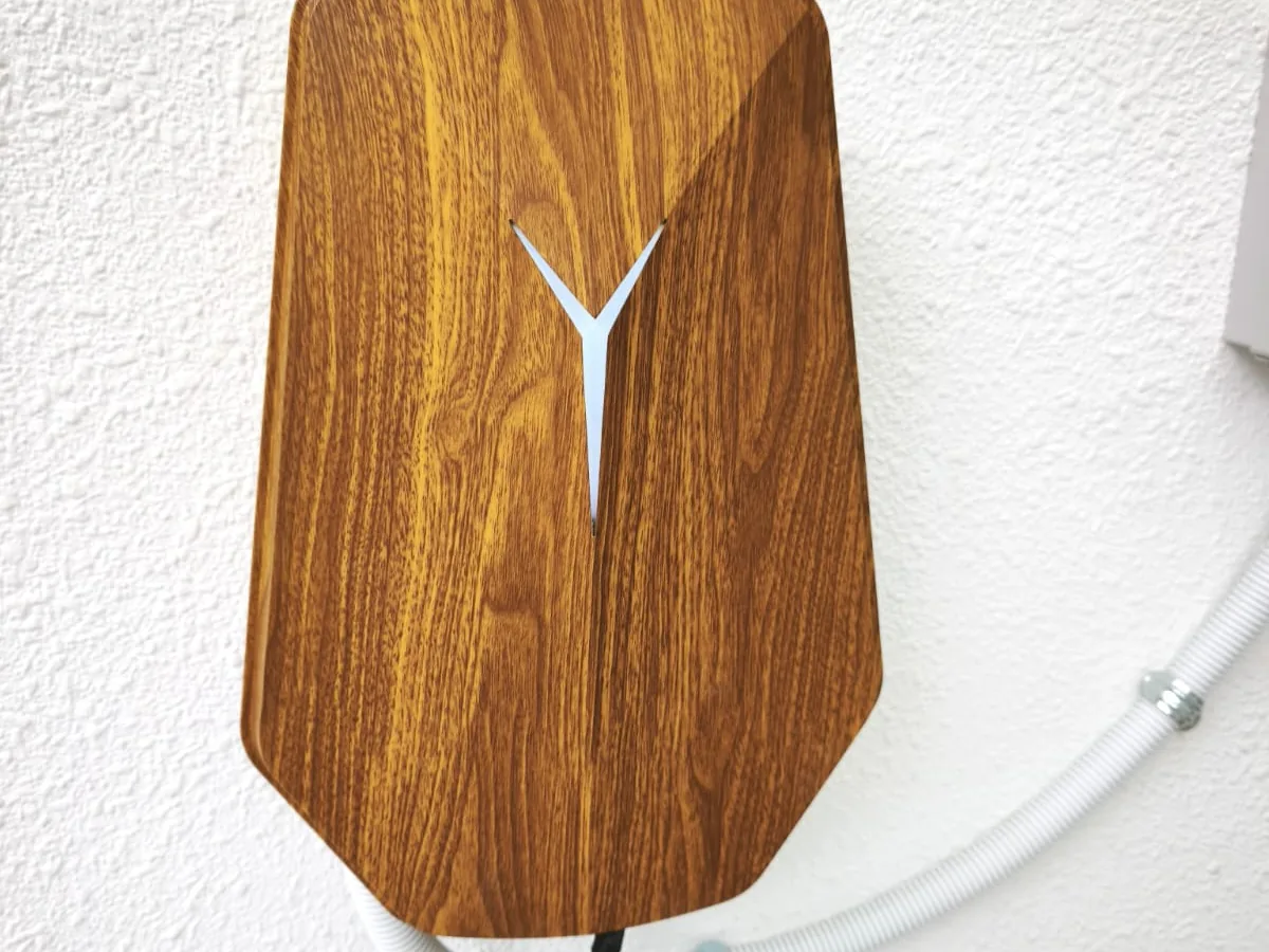 A wall charger with a wood-grain front panel and a white Y-shaped inset, mounted on a textured white wall with corrugated conduit entering from the right.