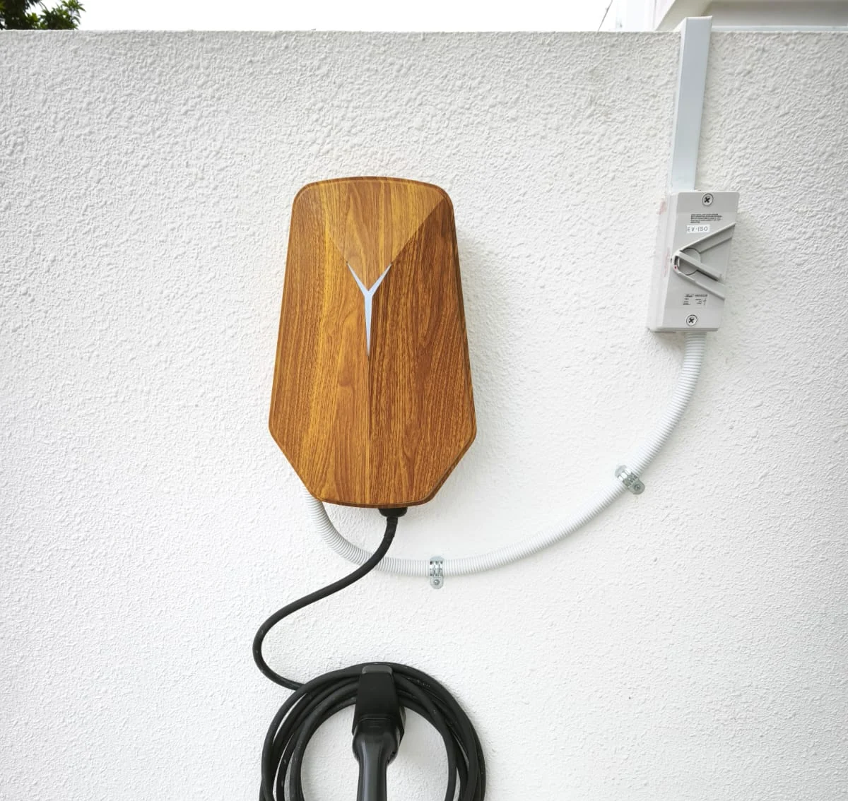 A wood-grain HiCi charger on a white rendered wall, its supply in white conduit running to an isolator, connector resting in a holster below.