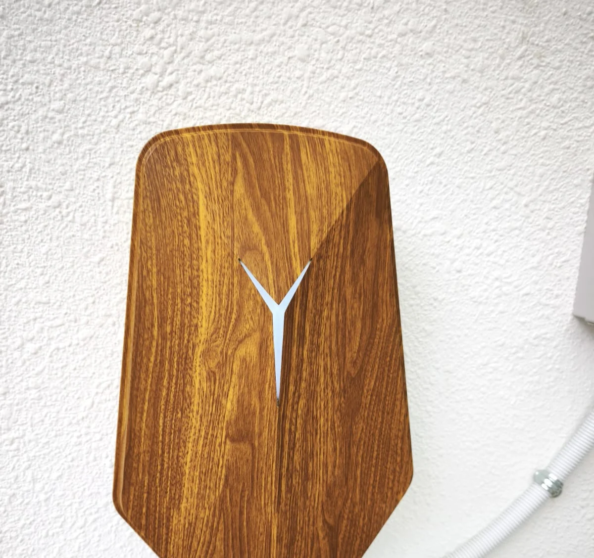 A wood-grain HiCi charger centred on a heavily textured white rendered wall, its white Y light and faceted shell filling the frame.