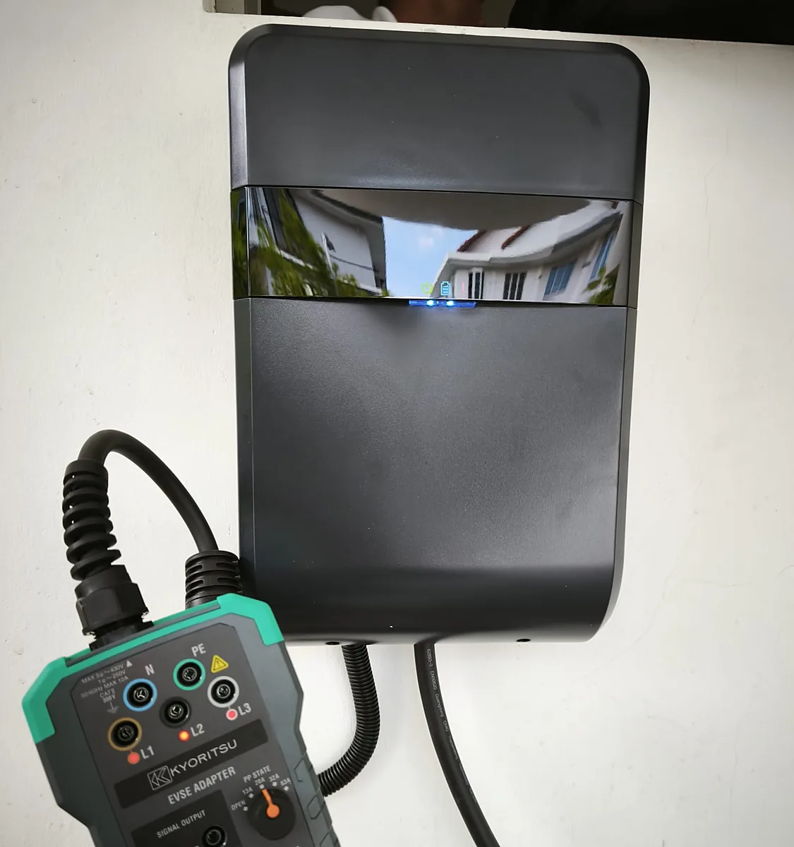 A black wall charger being tested, a multi-function test instrument connected to it by two leads.