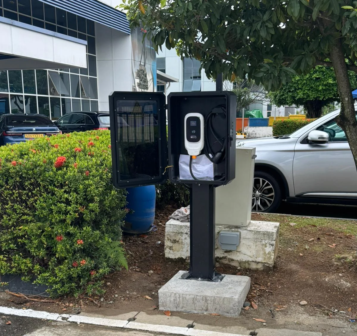 Two black post-mounted charger enclosures side by side on concrete plinths in a landscaped commercial car park.