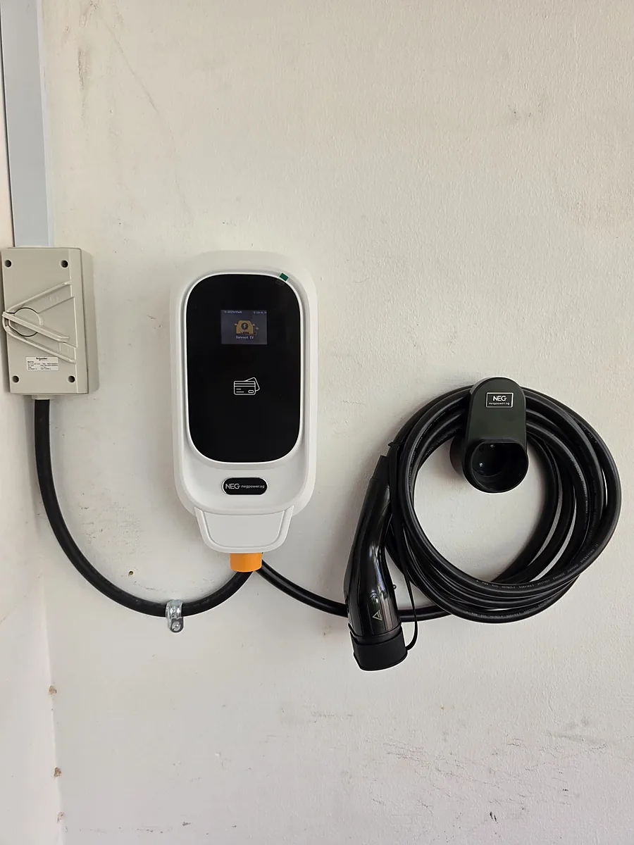 A white wall-mounted EV charger showing 'Connect EV' on its display, with an isolator switch to one side and the coiled lead stowed on a wall holster to the other.
