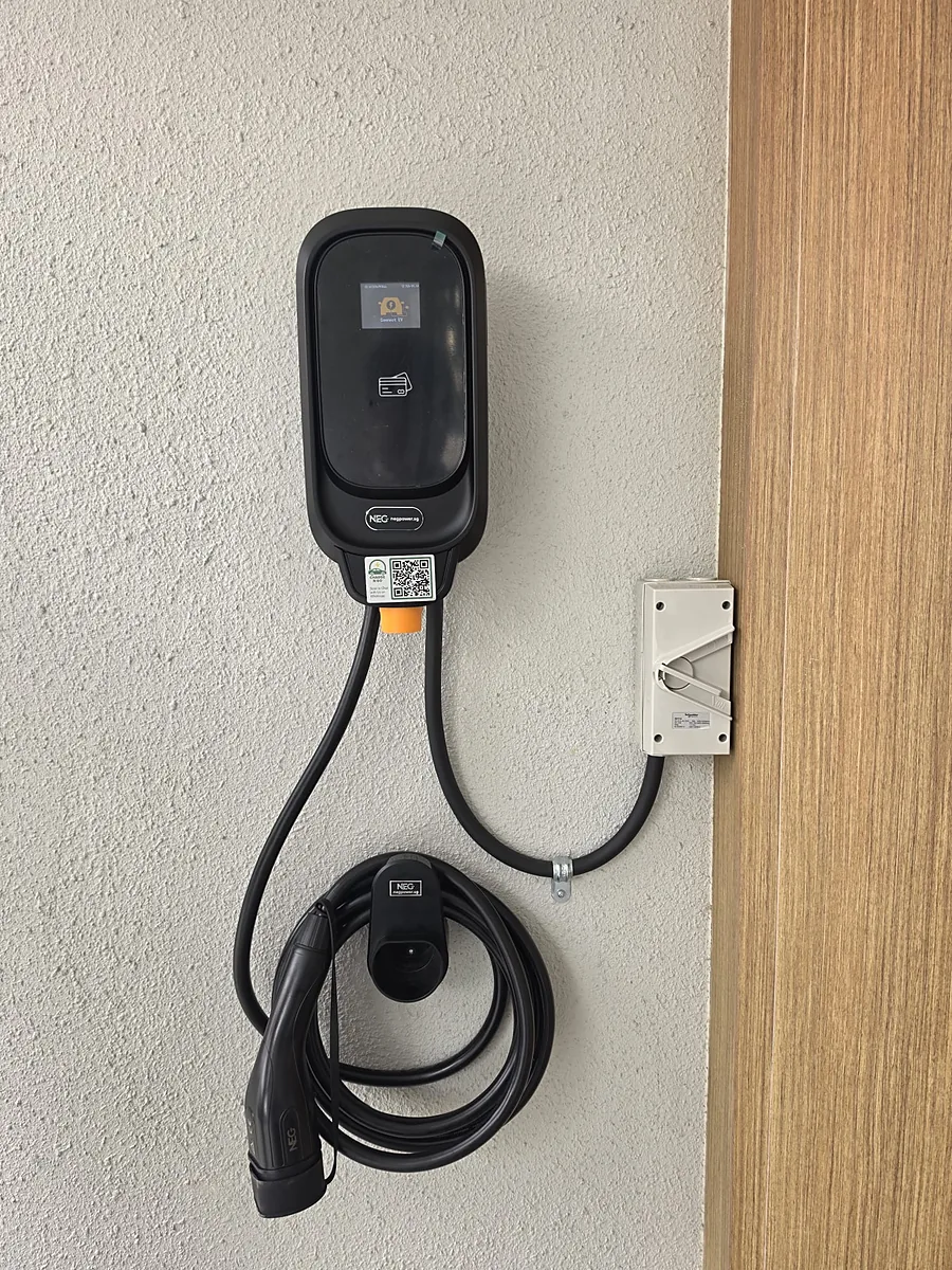 A black wall-mounted EV charger showing 'Connect EV' on a white textured wall, its coiled lead on a holster below and a weatherproof isolator to one side.