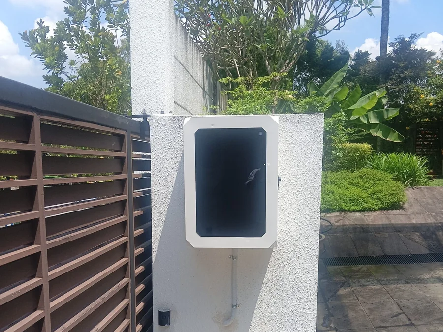 A white enclosure housing a charger, mounted on a rendered pillar beside timber screening and paving.