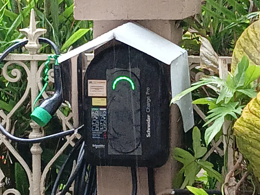 A Schneider Charge Pro on an exterior wall fitted with a sloped weather hood above it, planting either side and the connector stowed on its holster.