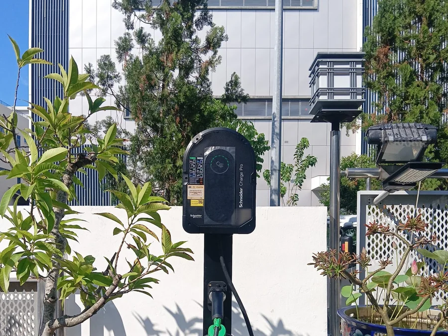 A Schneider Charge Pro mounted on a black standalone post set into paving, with the cable coiled at the base of the unit.